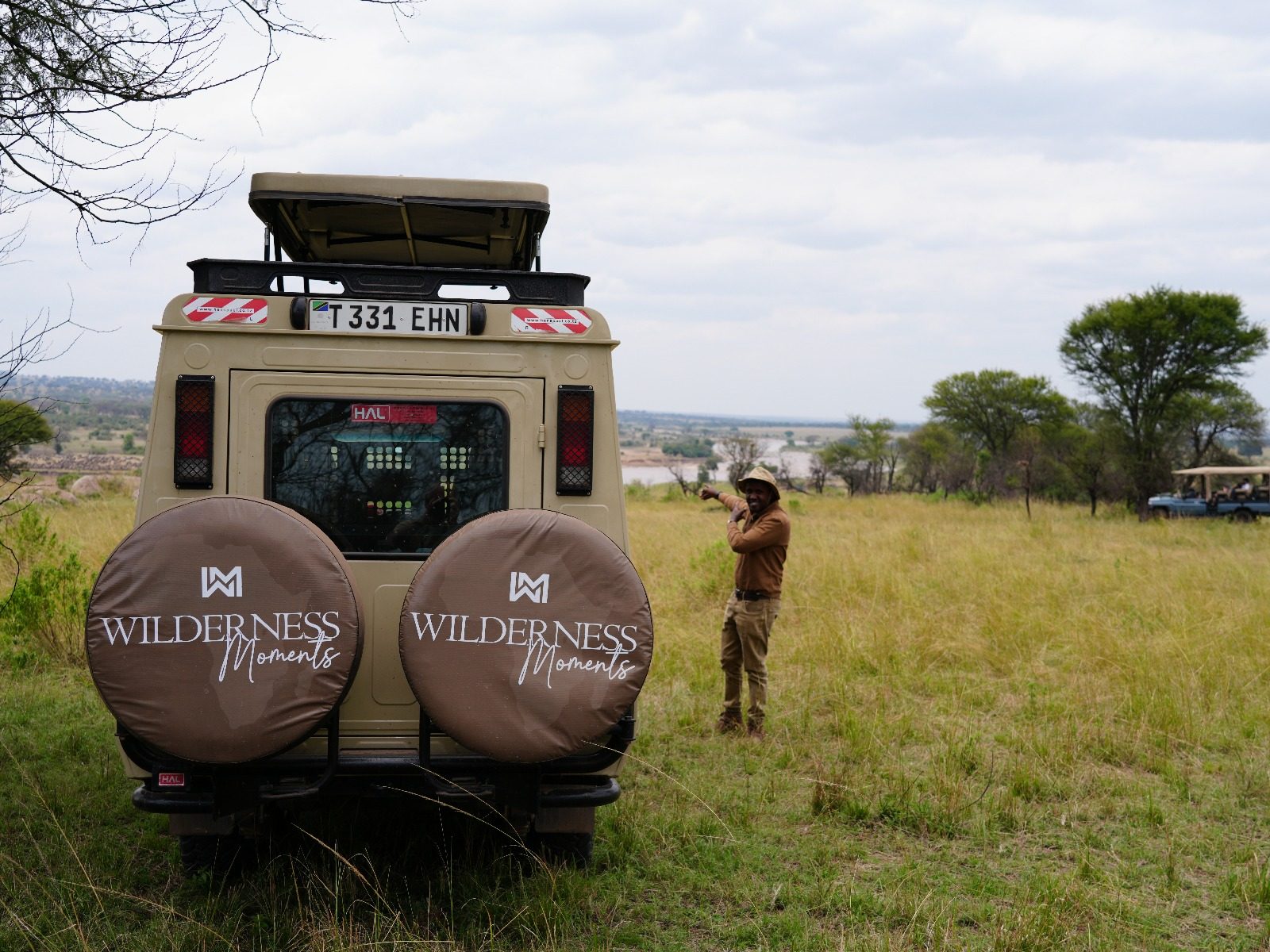 Wilderness Moments guide beside the Land Cruiser overlooking the Serengeti